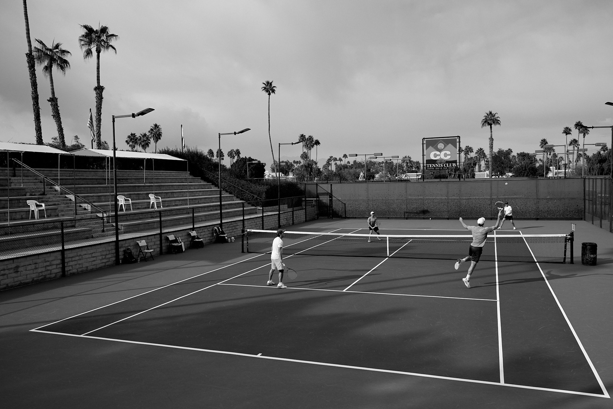 Doubles match in progress at CC Tennis Club, with the CC Tennis Club sign in the background